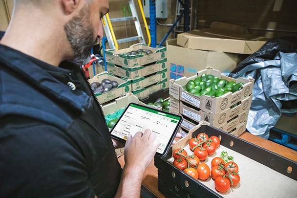 Fresho wholesale food order management system - Fresh Fruit and Vegetable supplier standing with iPad in hand using the Fresho app to check stock