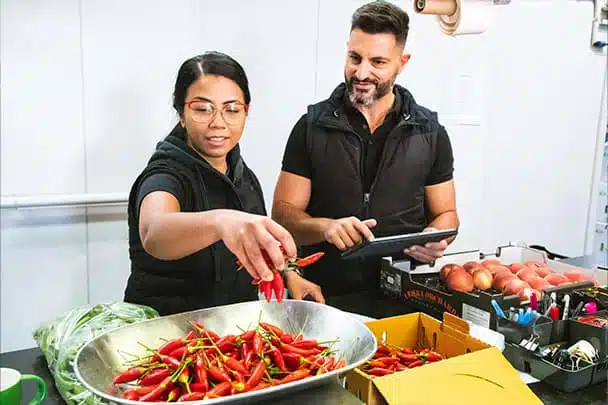 Fresho Software for fresh food wholesale suppliers and their customers - Two Fresho fresh fruit and veg employees weighing red chillies and packaging into a box using the Fresho app to ensure the correct delivery