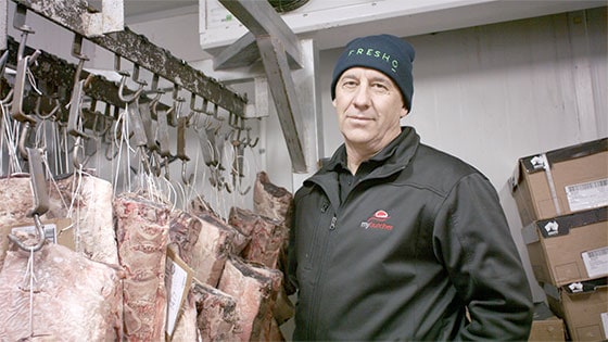 Fresho Software for fresh food wholesale suppliers and their customers - mybutcher managing director standing in a cool store with meat hanging from hooks