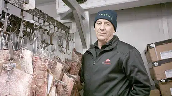 Fresho Software for fresh food wholesale suppliers and their customers - mybutcher managing director standing in a cool store with meat hanging from hooks