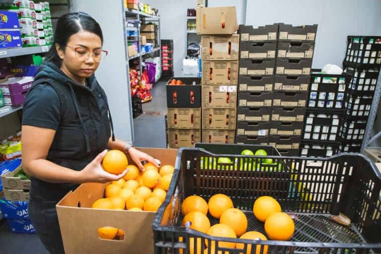 A female in a warehouse picking up oranges