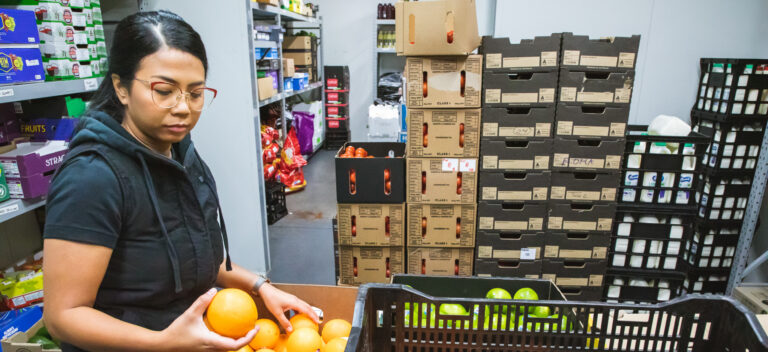 A female in a warehouse picking up oranges