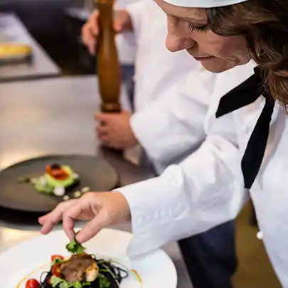 A female chef attending to a plate of food in a kitchen